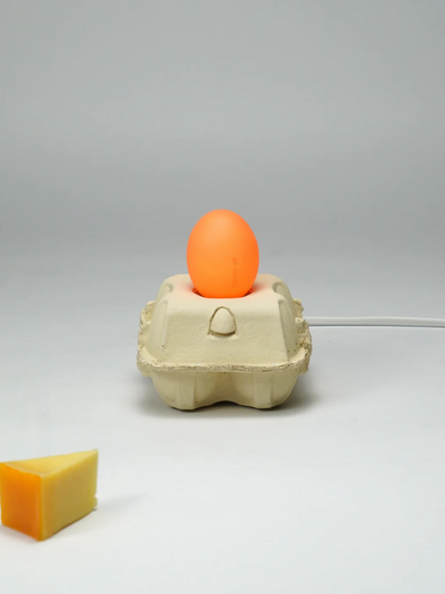 Nachhaltige LED-Lampe EggboxLAMP in Eiform mit sanftem orangefarbenem Leuchten und umweltfreundlichem Sockel