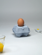EggboxLAMP Sky LED lamp met een ei op een grijze eierdoos, met aan/uit-schakelaar en glazen sap.