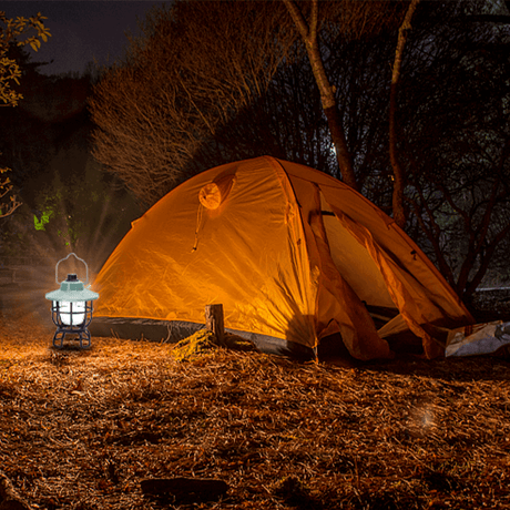 Aigostar wiederaufladbare LED-Campinglampe neben einem Zelt in einer dunklen Waldumgebung